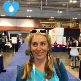 Person with braided hair and sunglasses on their head smiling at an indoor event or expo.