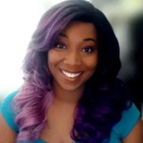Smiling person with long wavy hair fading from dark to purple, wearing a teal top.