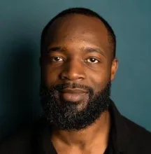 Smiling man with a full beard against a dark teal background.