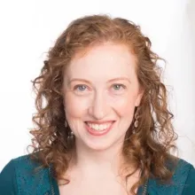 Smiling person with curly red hair against a light background.