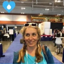 Person with braided hair and sunglasses on their head smiling at an indoor event or expo.