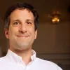Smiling man wearing a white button-up shirt indoors with a softly blurred background.