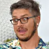Person with glasses and short hair making a surprised expression while wearing a colorful patterned shirt.